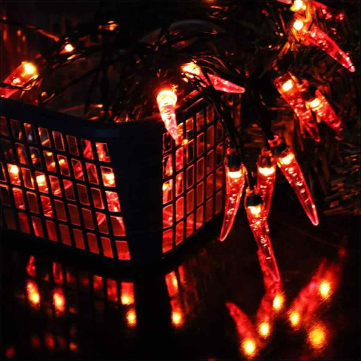 Nahaufnahme von roten chili-förmigen Lichterketten und einem dunklen quadratischen Objekt. Die Lichter spiegeln sich auf einer dunklen Oberfläche.