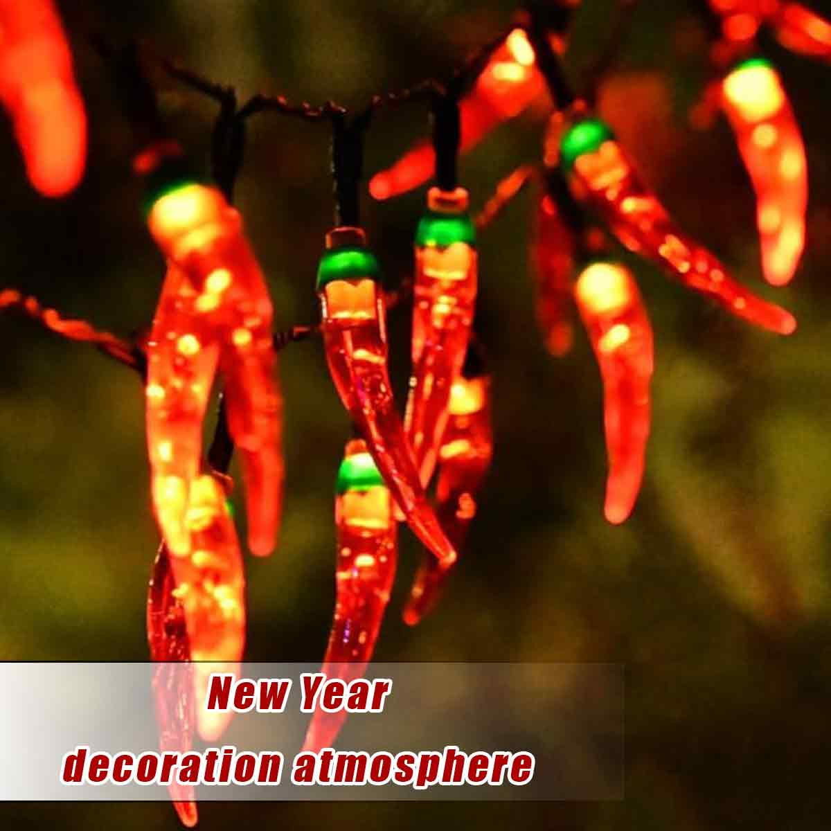 Nahaufnahme von chili-förmigen Lichtern. Die Lichter sind rot mit grünen Spitzen, auf schwarzen Drähten und schaffen eine festliche Atmosphäre.
