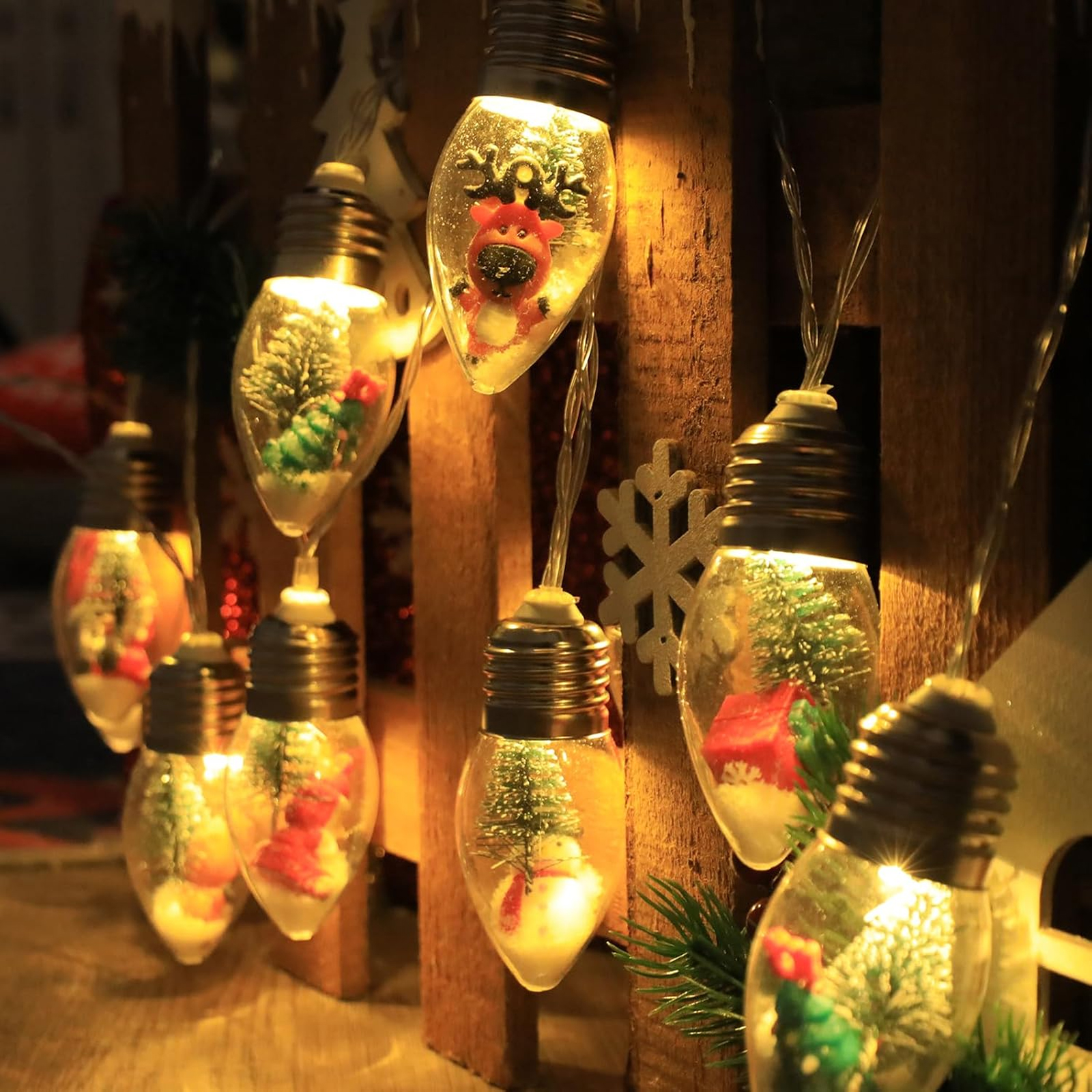 Weihnachtsbeleuchtung: Glühbirnen mit Miniatur-Szenen von Rentieren, Bäumen und Schnee. Holzuntergrund. Warmes Licht.