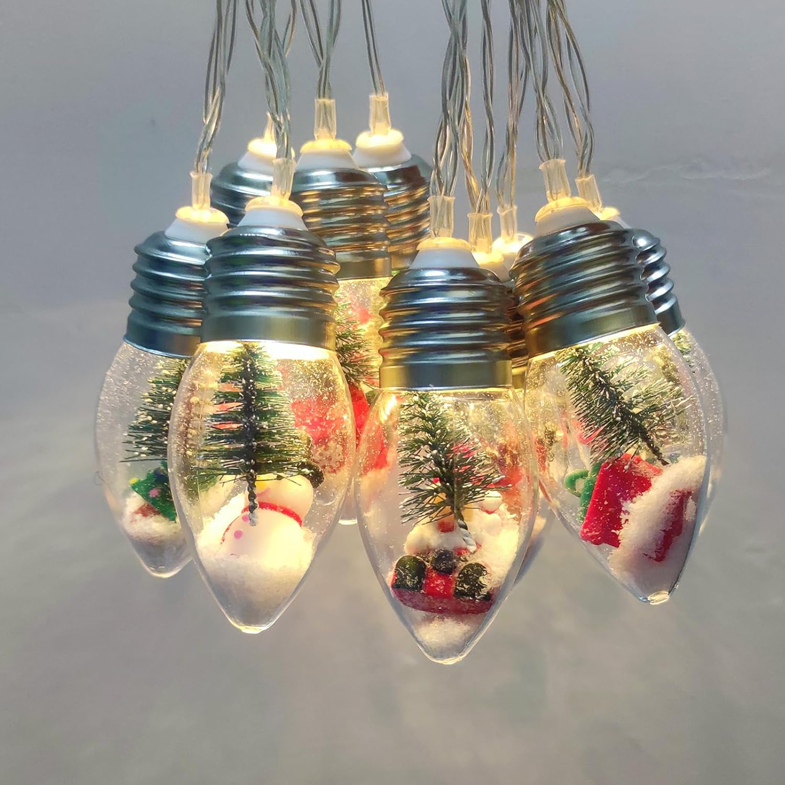 Lichterkette in Form von Glühbirnen. Jede Birne enthält eine Miniatur-Szene mit Baum und Schneemann.