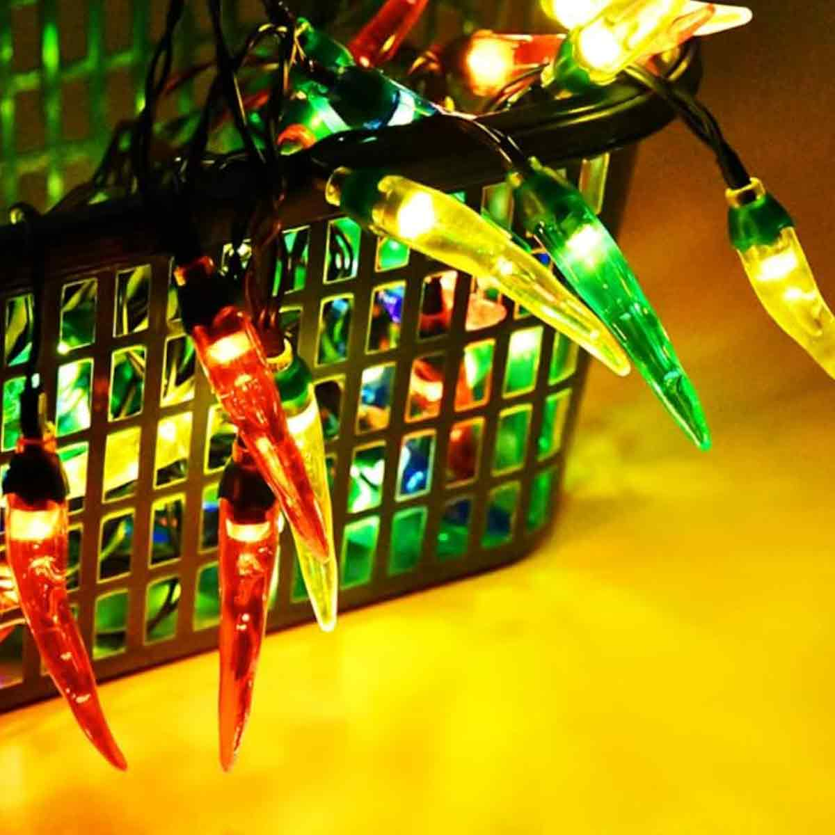 Chilischoten-förmige Lichterkette in einem Korb. Die Lichter sind rot, gelb und grün. Der Korb ist schwarz, auf einer gelben Oberfläche.