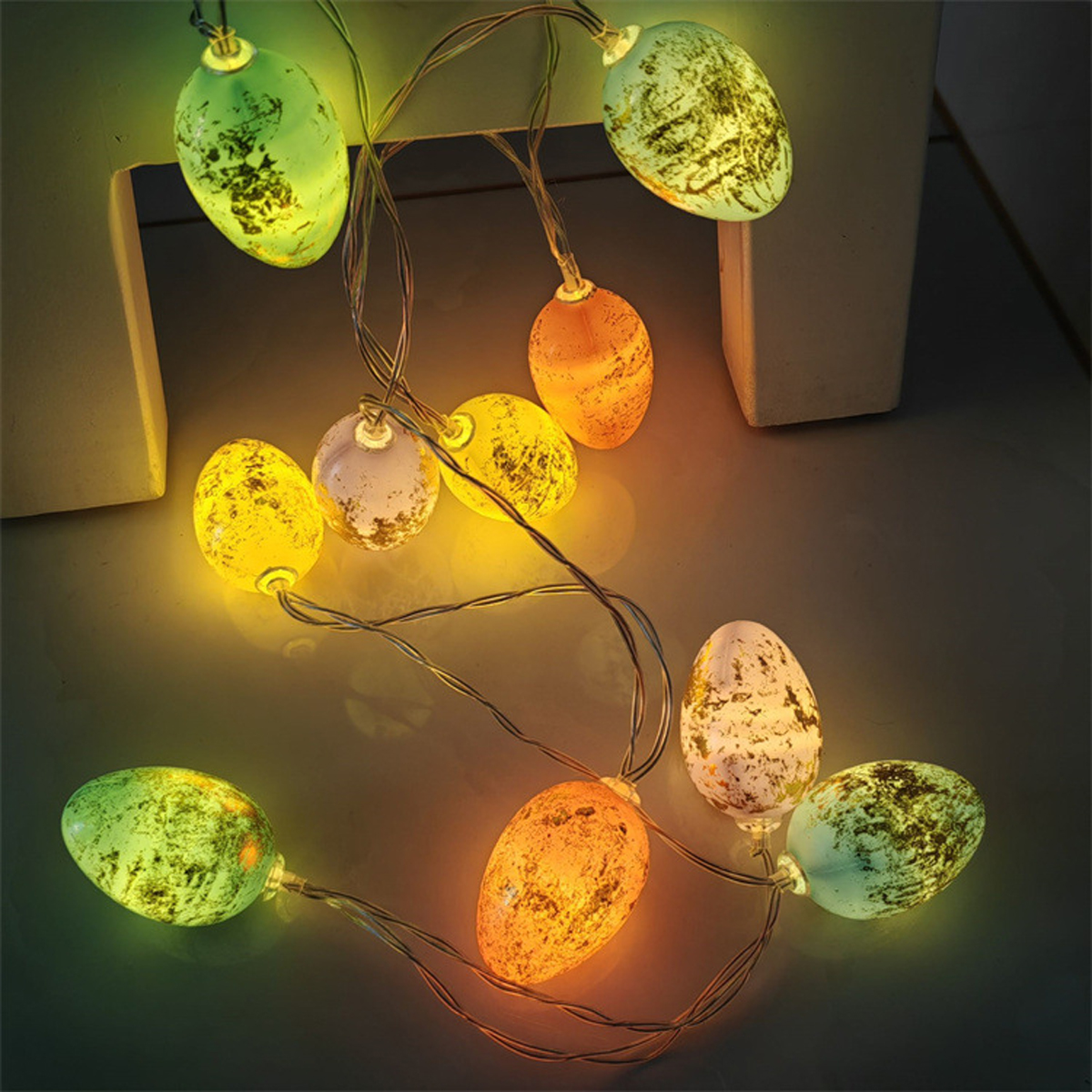 Eine Lichterkette mit leuchtenden eiförmigen Lichtern in verschiedenen Farben, darunter Grün, Gelb und Orange, auf einer dunklen Oberfläche.