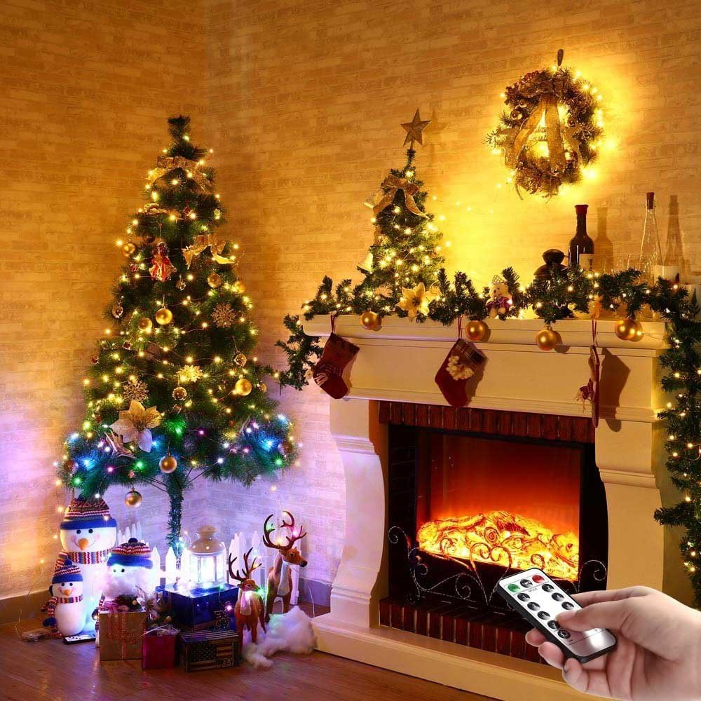 Weihnachtsszene mit beleuchteten Bäumen, Kamin, Strümpfen, Schneemännern, Rentieren und einer Hand mit Fernbedienung.