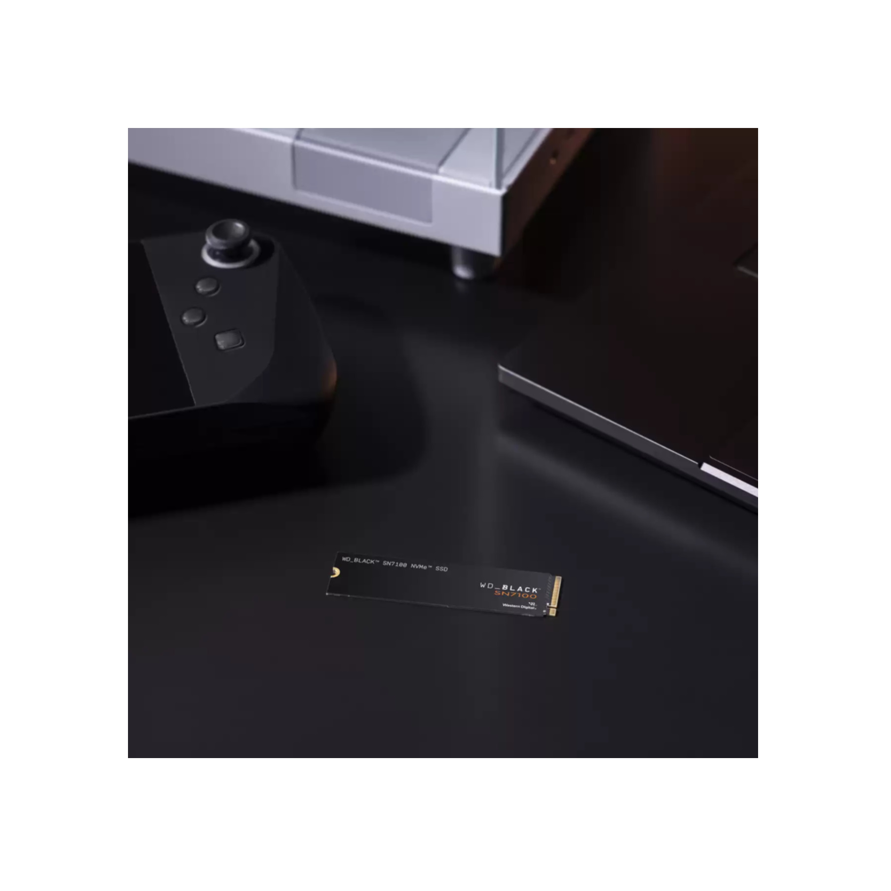 Dysk SSD WD_BLACK SN7100 na czarnej powierzchni. Kontroler do gier i laptop również widoczne w tle.