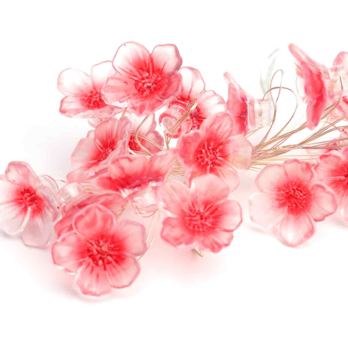 Nahaufnahme von rosa künstlichen Blumen auf weißem Hintergrund. Die Blumen haben mehrere Blütenblätter und sind an dünnen Drähten befestigt.
