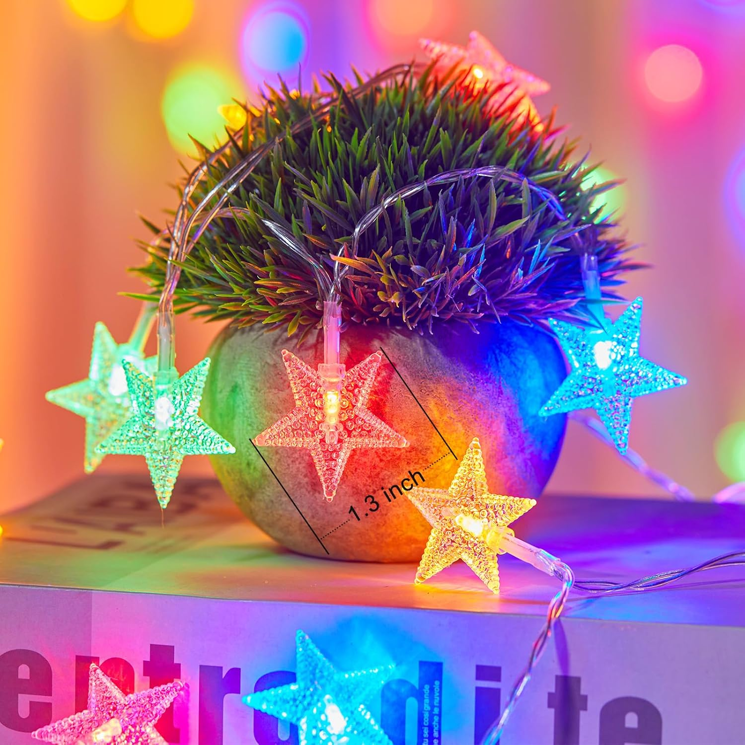 Ein kleiner Topf mit grünem Gras und sternförmigen Lichtern. Die Lichter haben verschiedene Farben, mit einem weichen, farbenfrohen Hintergrund.