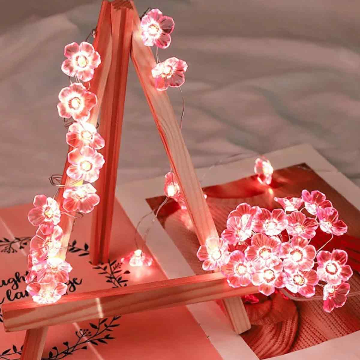 Eine hölzerne Staffelei, die mit rosa Blumenlichtern geschmückt ist. Lichter leuchten und beleuchten die Blumen. Der Hintergrund ist unscharf.