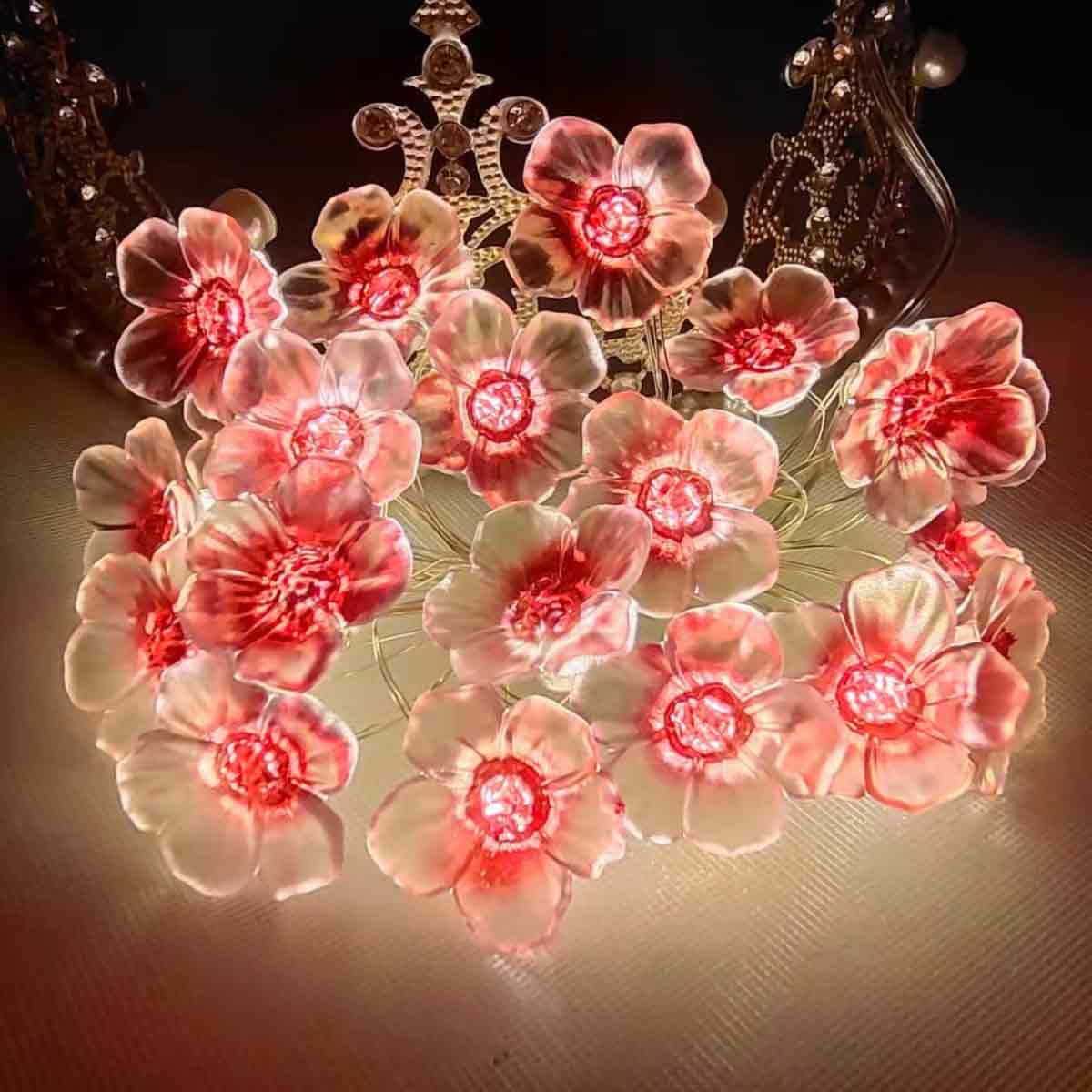 Nahaufnahme von dekorativen Blumen mit roten Zentren und rosa Blütenblättern auf einer reflektierenden Oberfläche mit Verzierungen im Hintergrund.
