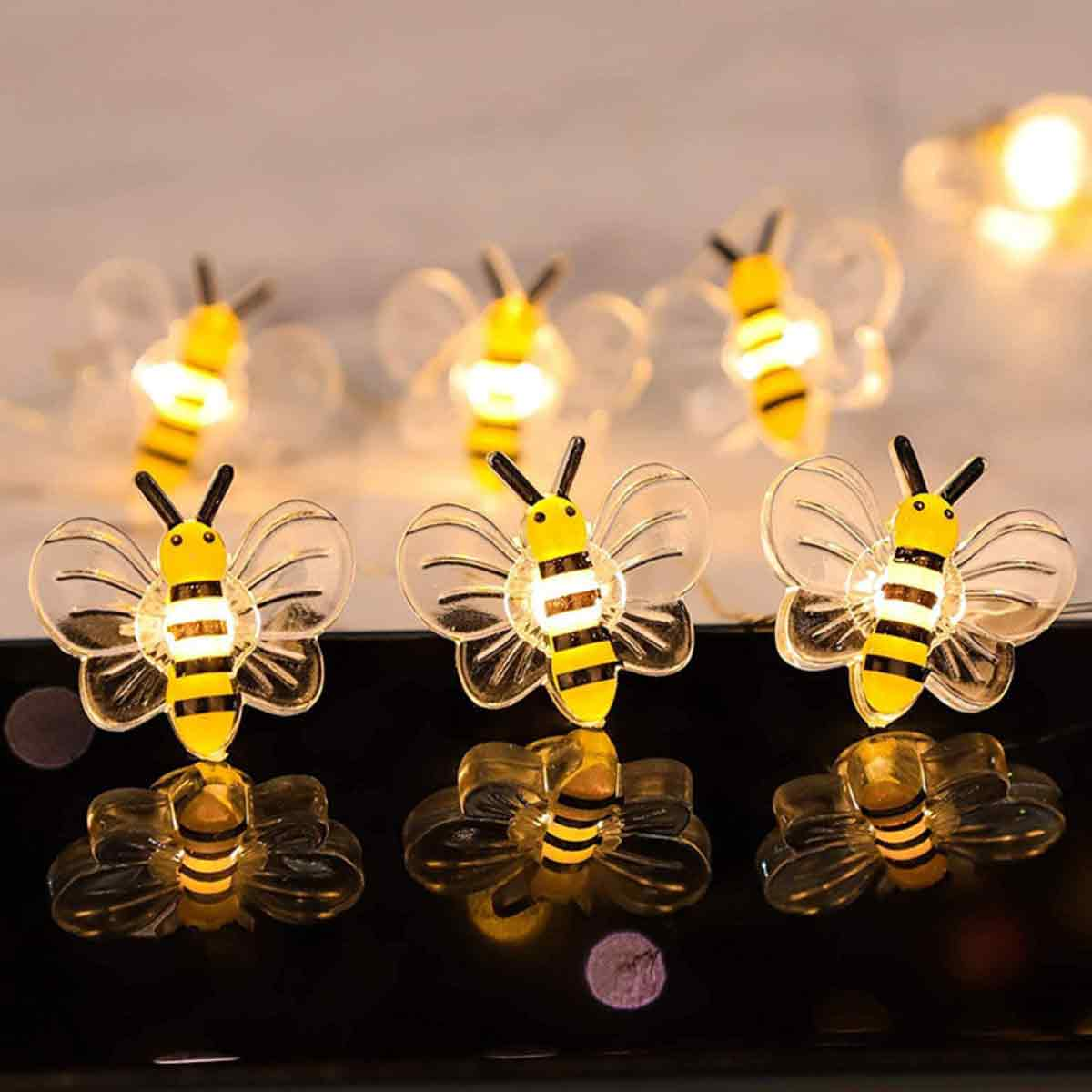 Lichterkette in Bienenform. Die Bienen haben gelb-schwarze Streifen, klare Flügel und sind beleuchtet. Sie befinden sich auf dunkler Oberfläche.