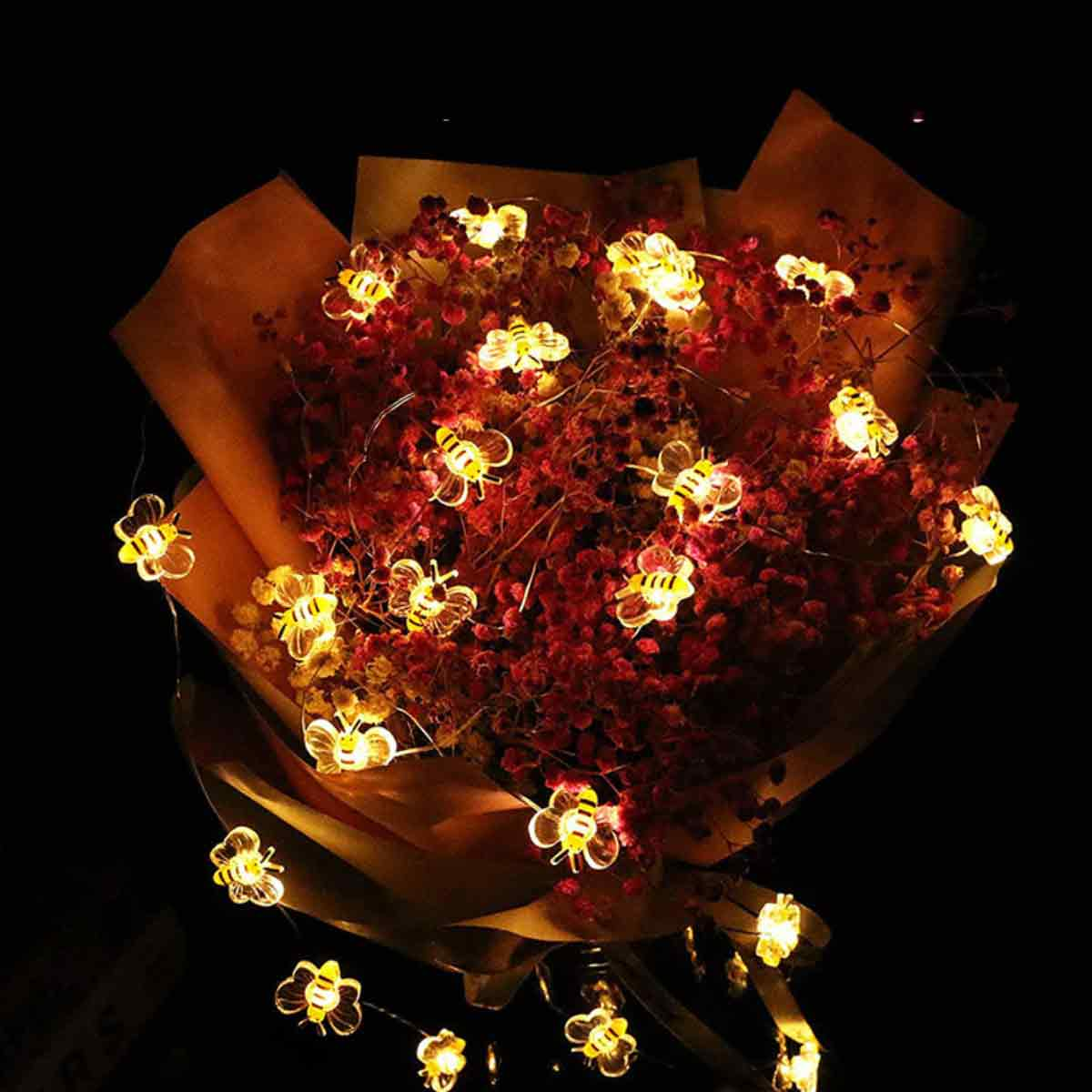 Ein Blumenstrauß aus roten Blumen, eingewickelt in braunes Papier, verziert mit bienenförmigen Lichterketten.