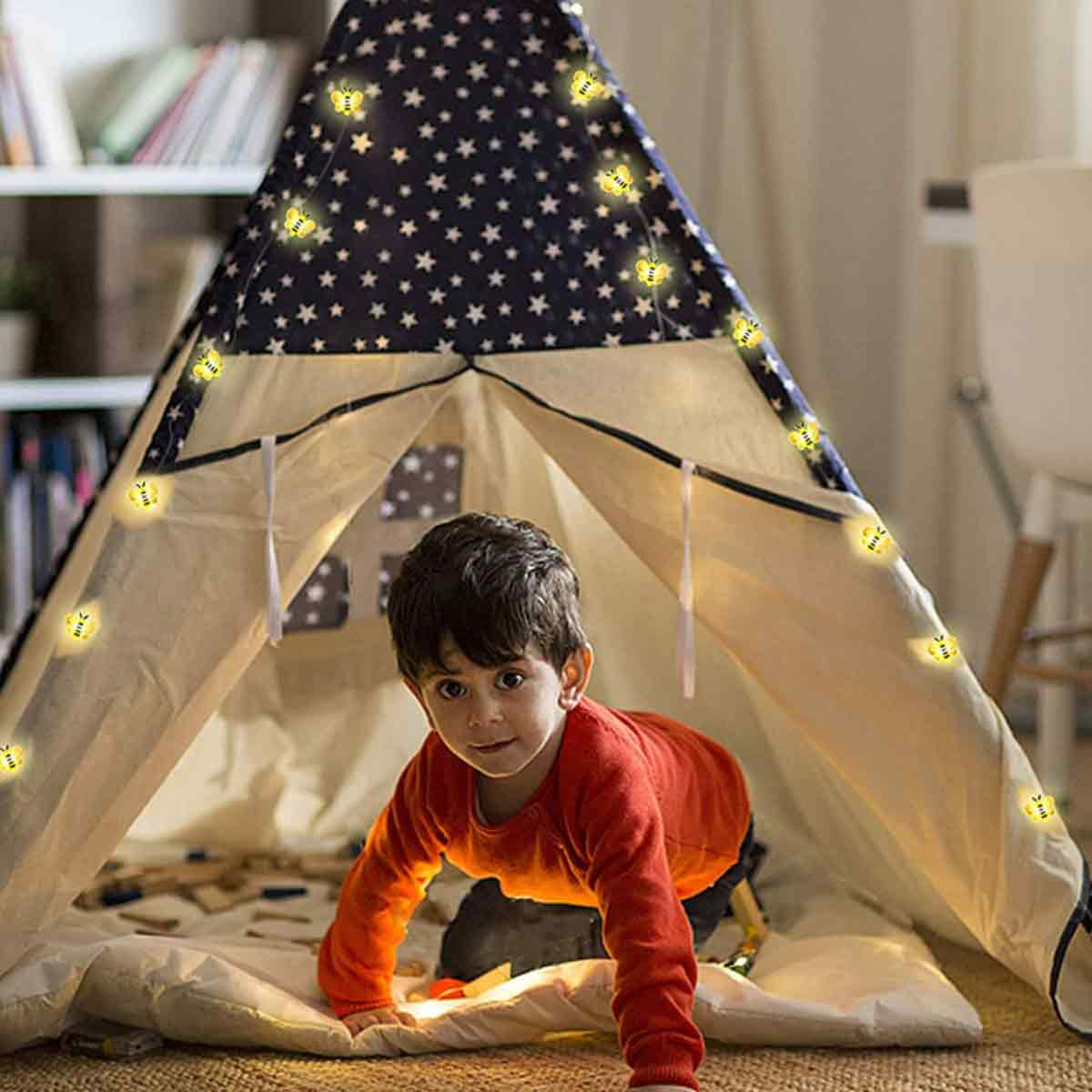 Ein kleiner Junge krabbelt aus einem mit Sternen und Lichtern geschmückten Tipi-Zelt. Er trägt ein rotes Hemd und schaut direkt in die Kamera.