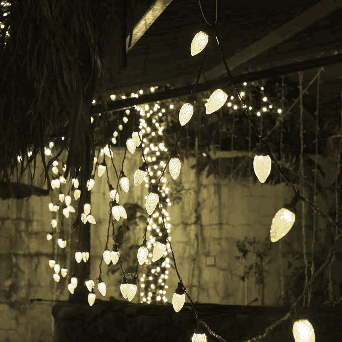 Lichterketten beleuchten einen Außenbereich. Warmweiße Glühbirnen hängen in Schnüren, weitere Lichter im Hintergrund. Sepia-Ton.