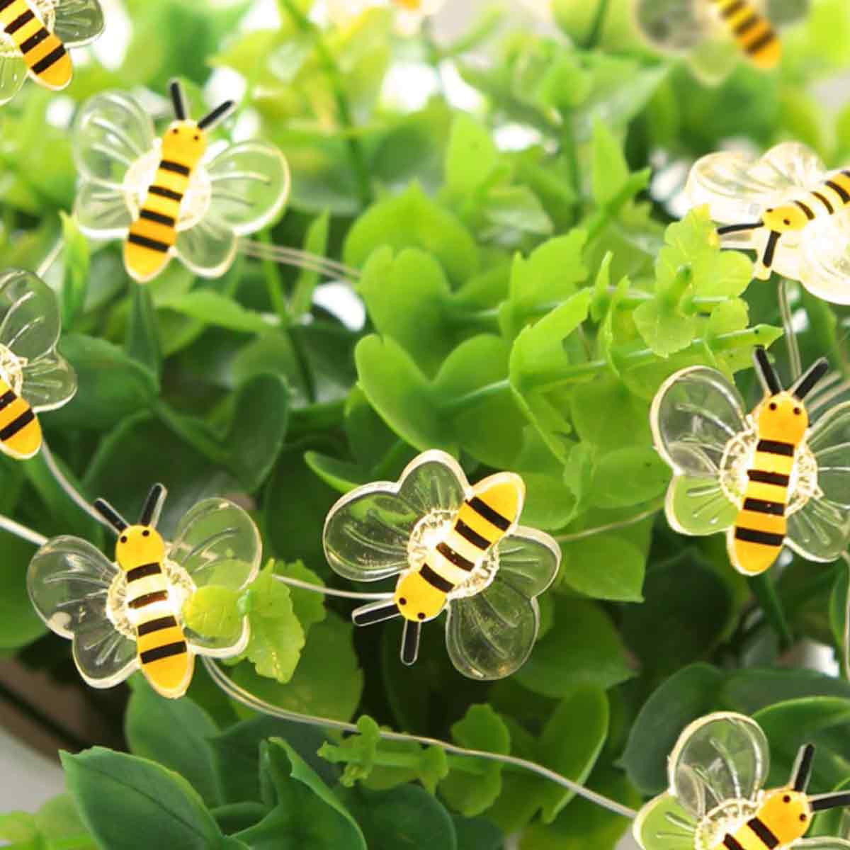 Kette aus dekorativen Bienenlichtern auf grünem Laub. Jede Biene hat gelbe und schwarze Streifen, klare Flügel und schwarze Antennen.