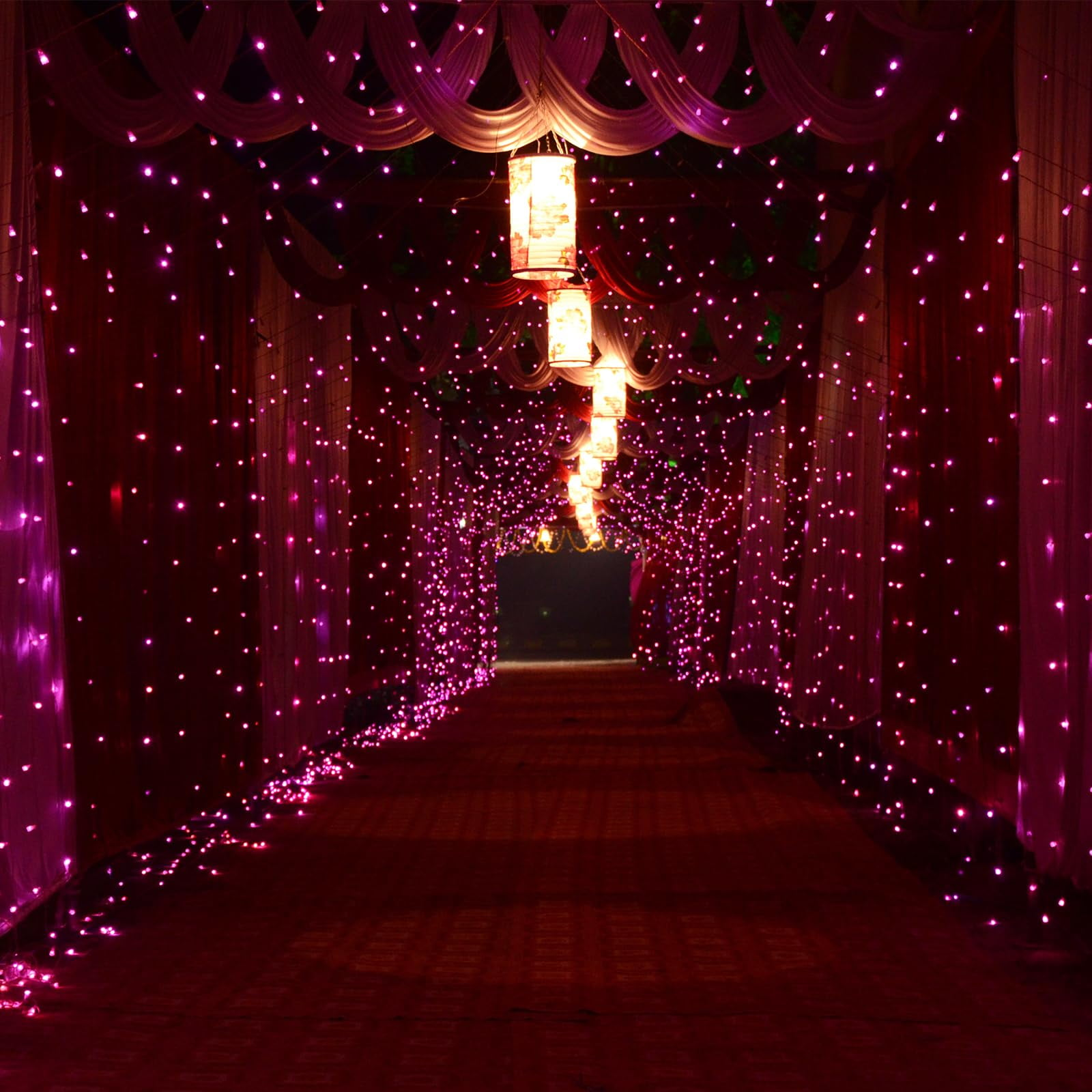 Ein beleuchteter Tunnel mit rosa Lichtern und Laternen. Roter Teppich und Vorhänge führen zu einem dunklen Ende.