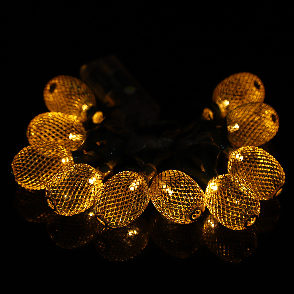 Eine Lichterkette aus goldenen, mit Maschen bedeckten Lichtern leuchtet vor schwarzem Hintergrund. Die Lichter spiegeln sich. Die Szene ist dunkel, mit den Lichtern als Fokus.