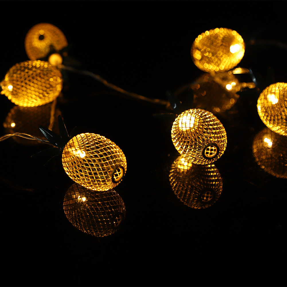 Lichterketten in Ananasform. Jedes Licht ist ein goldener Metallkäfig mit warmem Glanz. Sie spiegeln sich auf einer schwarzen Oberfläche.