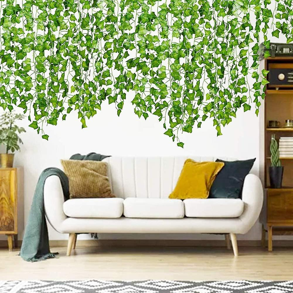 Ein weißes Sofa mit bunten Kissen steht unter hängenden grünen Ranken. Ein Teppich, Holzregale und Pflanzen sind ebenfalls im Raum.