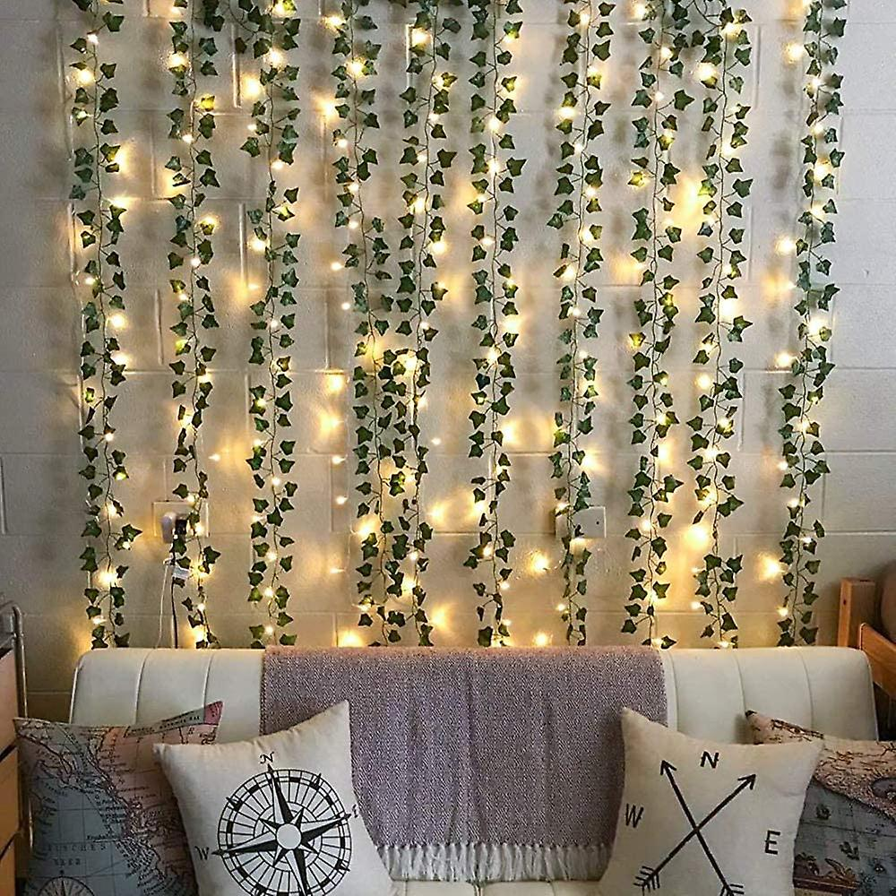 Wand mit Efeu und Lichtern dekoriert. Eine weiße Couch hat Kissen mit Kompass- und Kartendesigns. Eine Decke bedeckt die Couch.