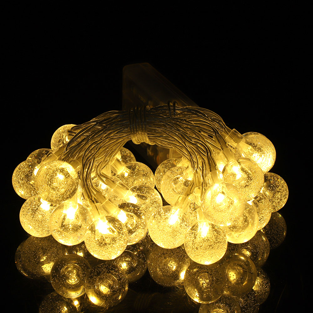 Lichterketten mit leuchtenden, klaren, blasenartigen Glühbirnen, die eine warme, beleuchtete Anzeige vor einem schwarzen, reflektierenden Hintergrund erzeugen.