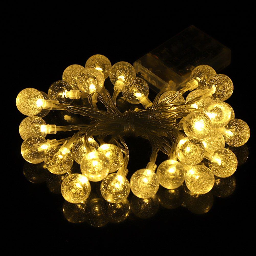 Lichterkette aus leuchtenden Kugellichtern auf schwarzem Untergrund. Die Lichter sind warmgelb. Ein Batteriepack befindet sich im Hintergrund.