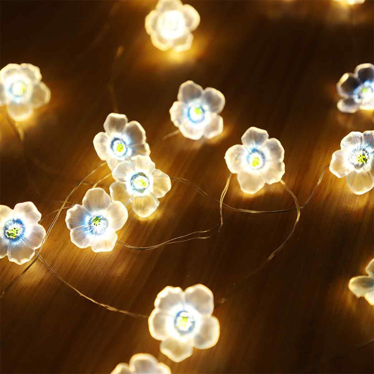 Nahaufnahme von blütenförmigen Lichterketten. Die Lichter sind weiß mit blau-gelbem Zentrum und liegen auf einer Holzoberfläche.