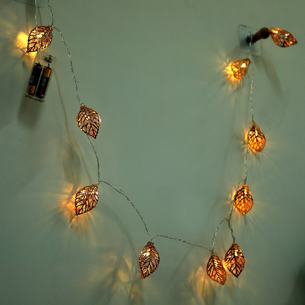 Lichterketten mit blattförmigen Lampen hängen an einer Wand. Die Blätter sind orange und die Lichter sind an. Links ist ein Akku.