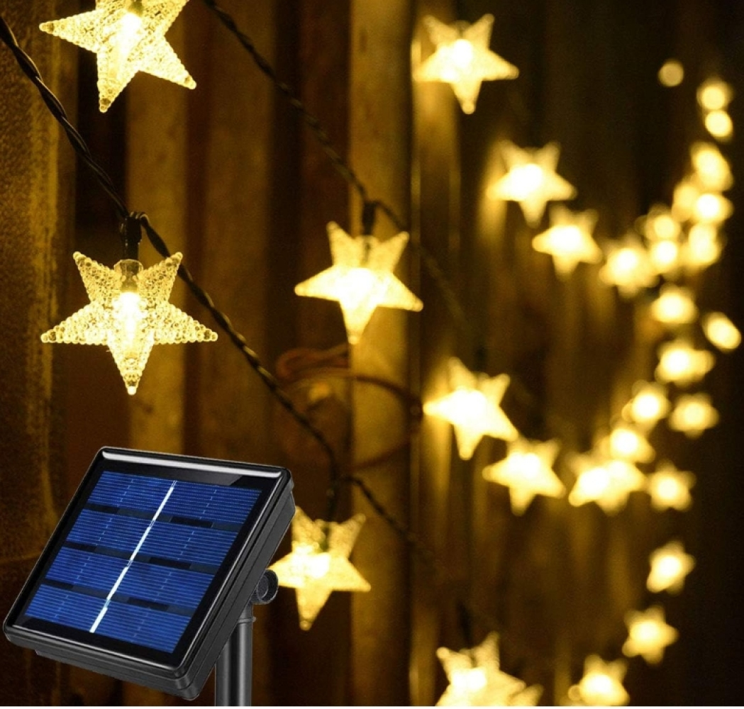 Lichterketten mit sternförmigen Glühbirnen. Im Vordergrund befindet sich ein Solarpanel. Warmes Licht vor dunklem Hintergrund.
