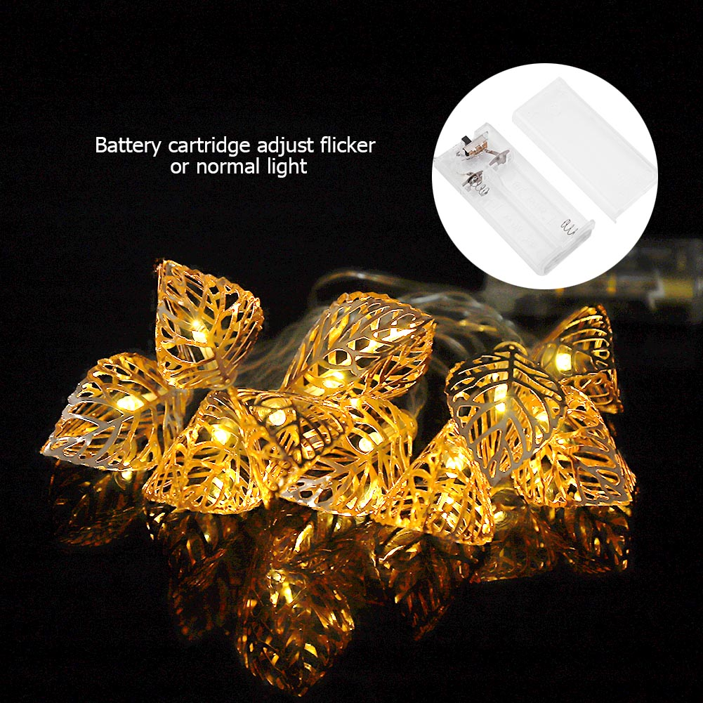 Goldene blattförmige Lichter mit einem Akkupack. Die Lichter spiegeln sich auf einer schwarzen Oberfläche. Text: Batteriepatrone, flackern oder normales Licht einstellen.