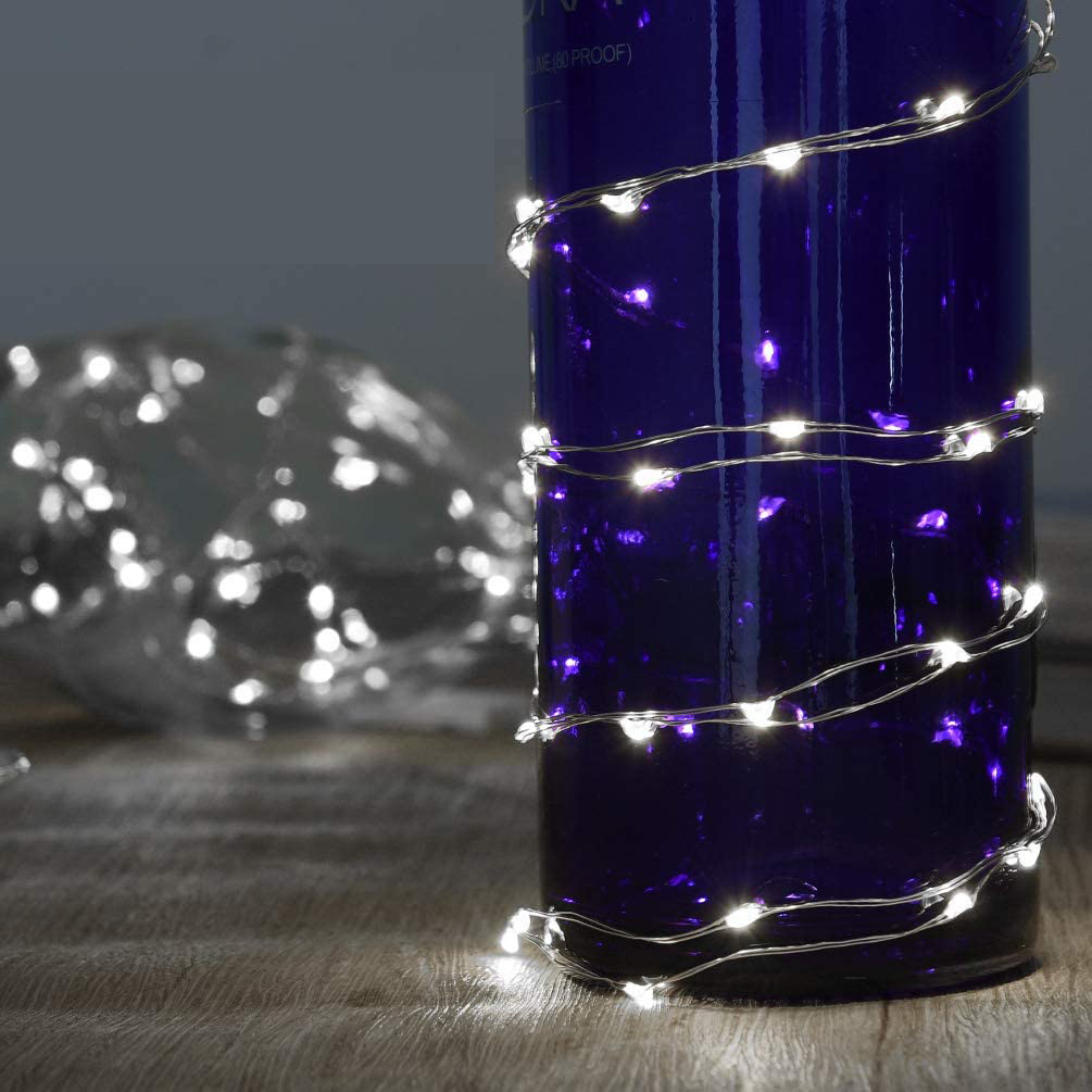 Eine blaue Flasche, umwickelt mit Lichterketten. Eine weitere Flasche mit Lichtern ist im Hintergrund unscharf. Die Oberfläche ist aus Holz.