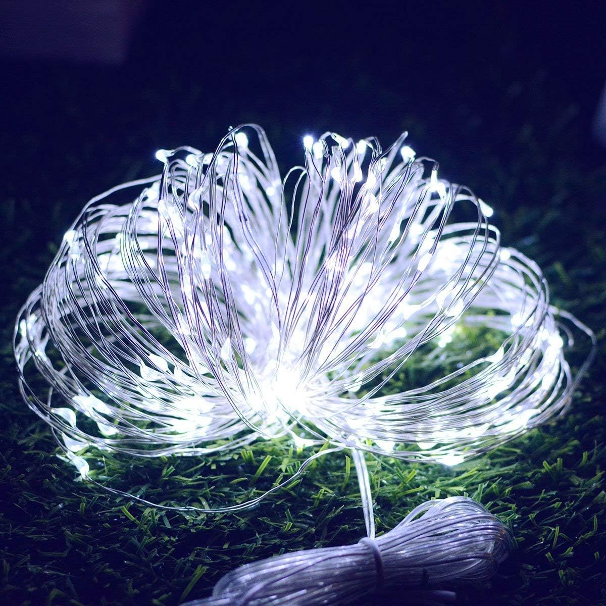 Lichterketten, weiße LEDs, auf grünem Gras aufgerollt. Die Lichter sind hell, das Gras dunkelgrün.