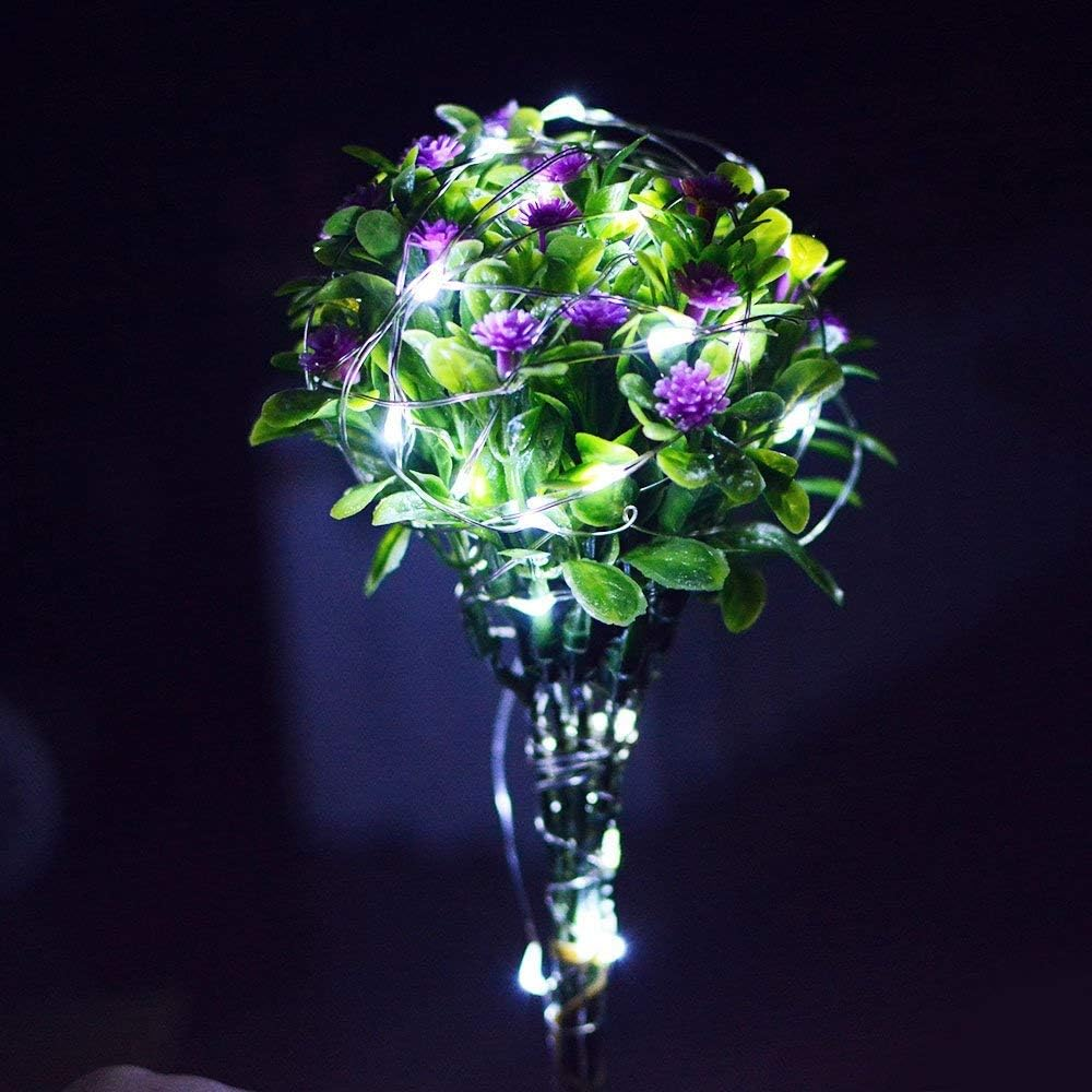 Ein Strauß aus grünen Blättern und lila Blumen, umwickelt mit Lichterketten in einer Vase vor dunklem Hintergrund.