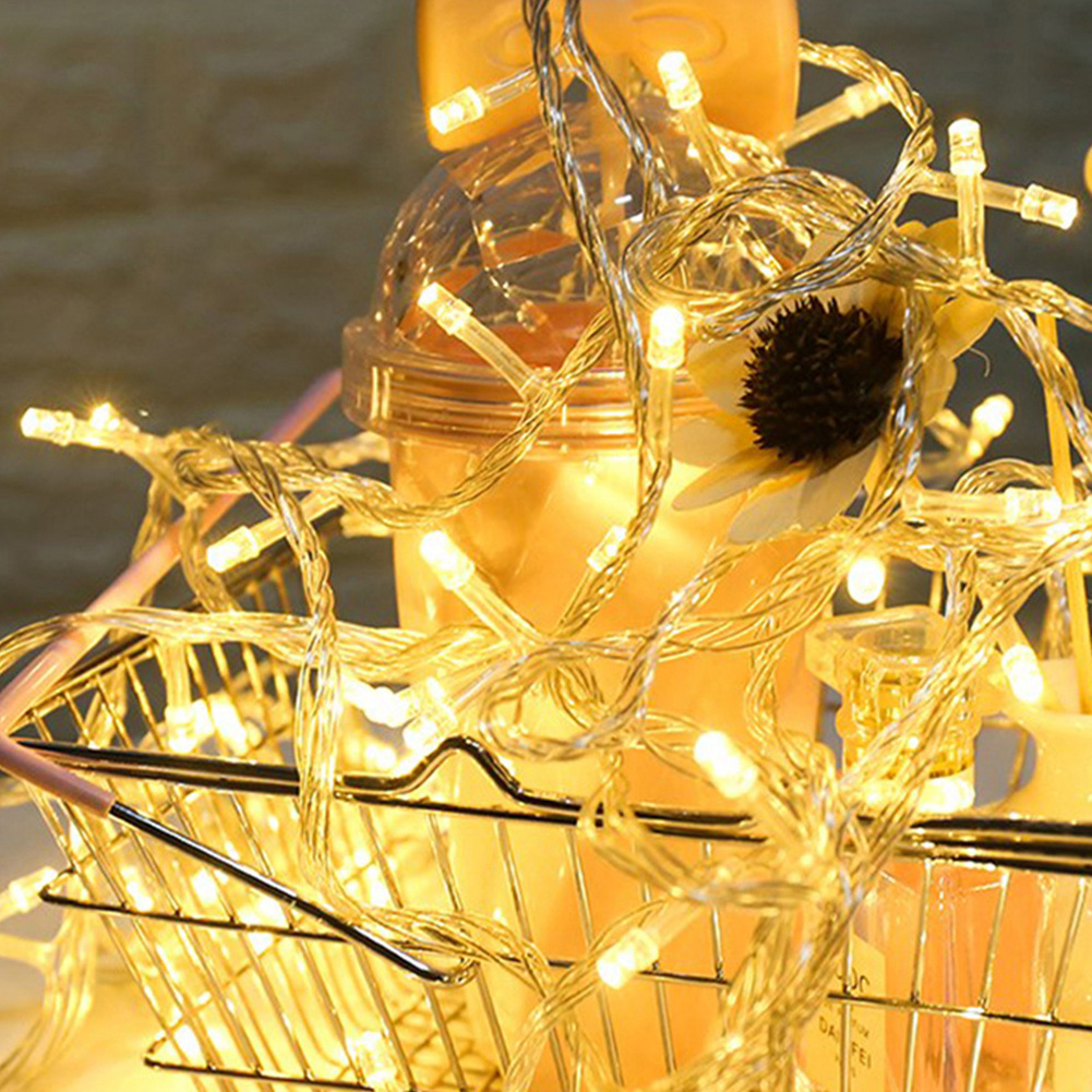 Nahaufnahme von Lichterketten. Ein Drahtkorb enthält ein Getränk und eine Sonnenblume. Die Lichter sind warm und golden.