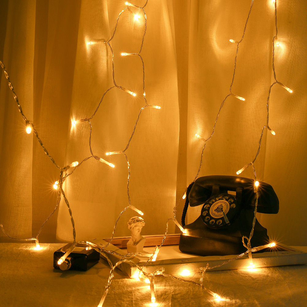 Ein schwarzes Vintage-Wählscheibentelefon steht auf einem Tisch mit Lichterketten und einer kleinen Büstenstatue vor einem Vorhang.