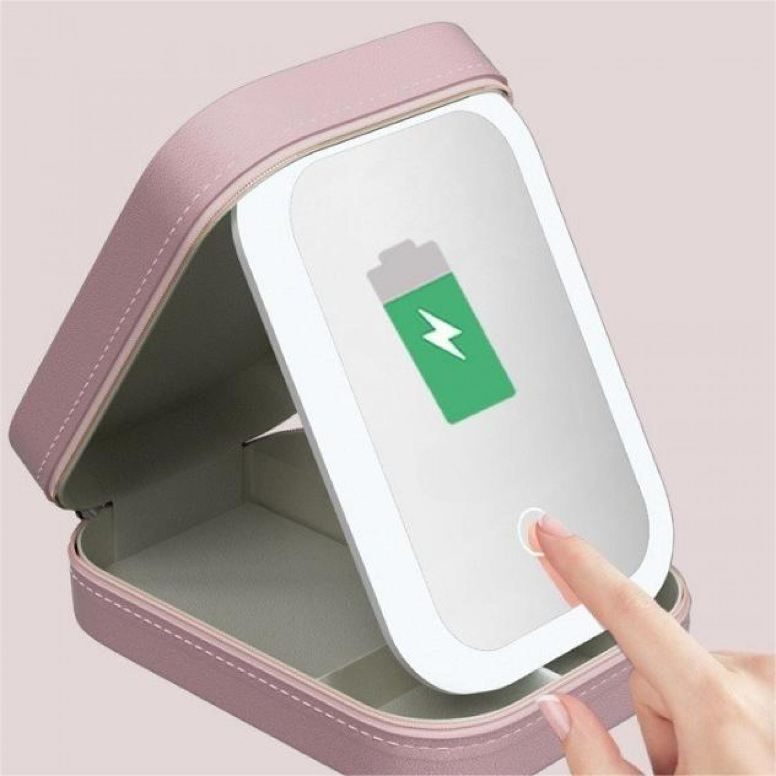 Ein rosa Make-up-Etui ist geöffnet und zeigt einen Spiegel mit einem grünen Batteriesymbol. Ein Finger berührt den Spiegel.