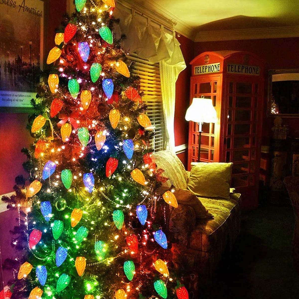 Ein geschmückter Weihnachtsbaum mit bunten Lichtern. Eine rote Telefonzelle und ein Sofa befinden sich im Hintergrund.