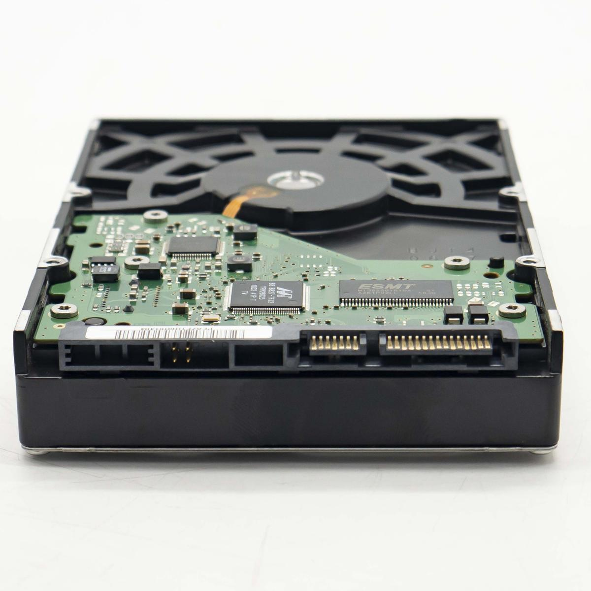 Un disco rigido con circuito stampato verde e involucro nero, componenti visibili. La parte superiore ha uno sfiato. Sfondo bianco.