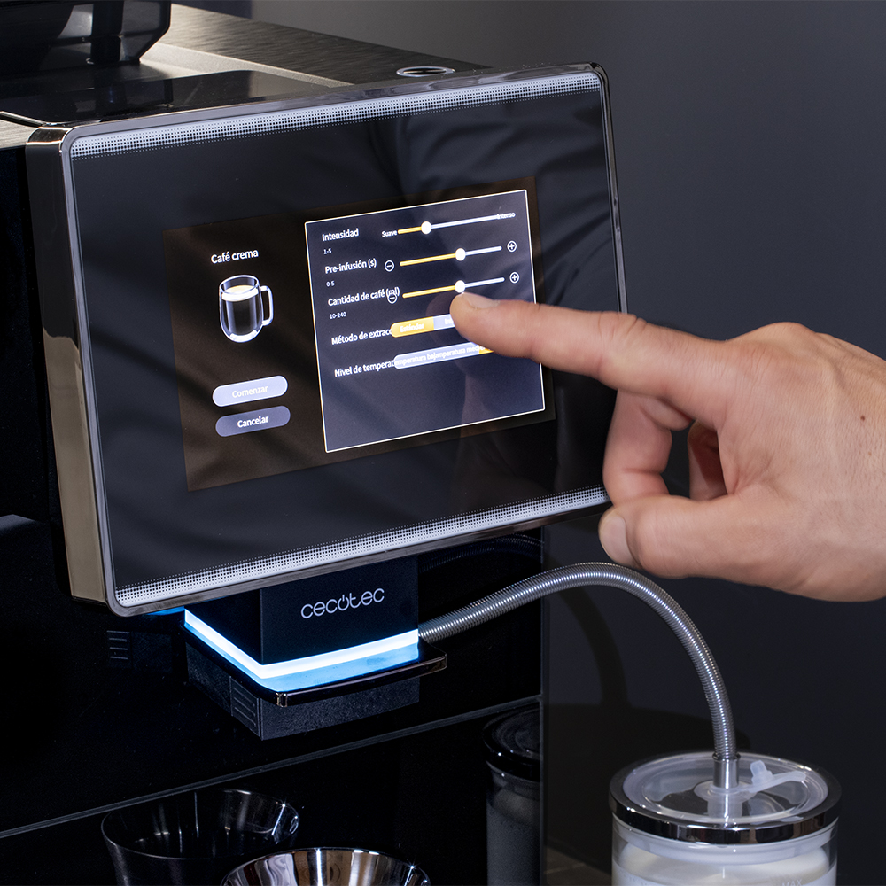 Una mano toca la pantalla de una cafetera. La pantalla muestra ajustes de café. La máquina tiene un tubo plateado conectado a un tarro.