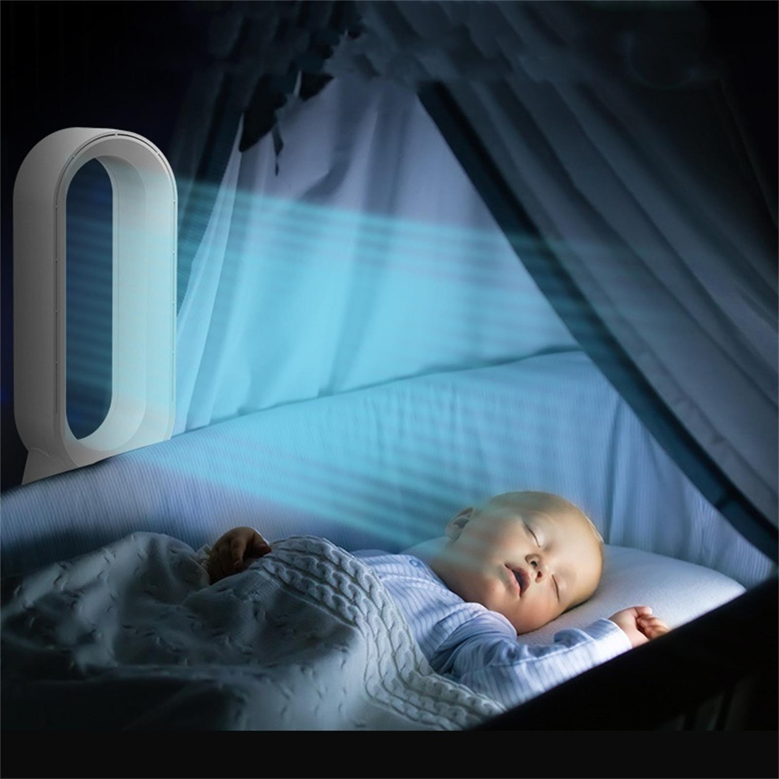 Ein Baby schläft in einem Kinderbett, beleuchtet von blauem Licht eines Ventilators. Links ist ein weißer Ventilator.