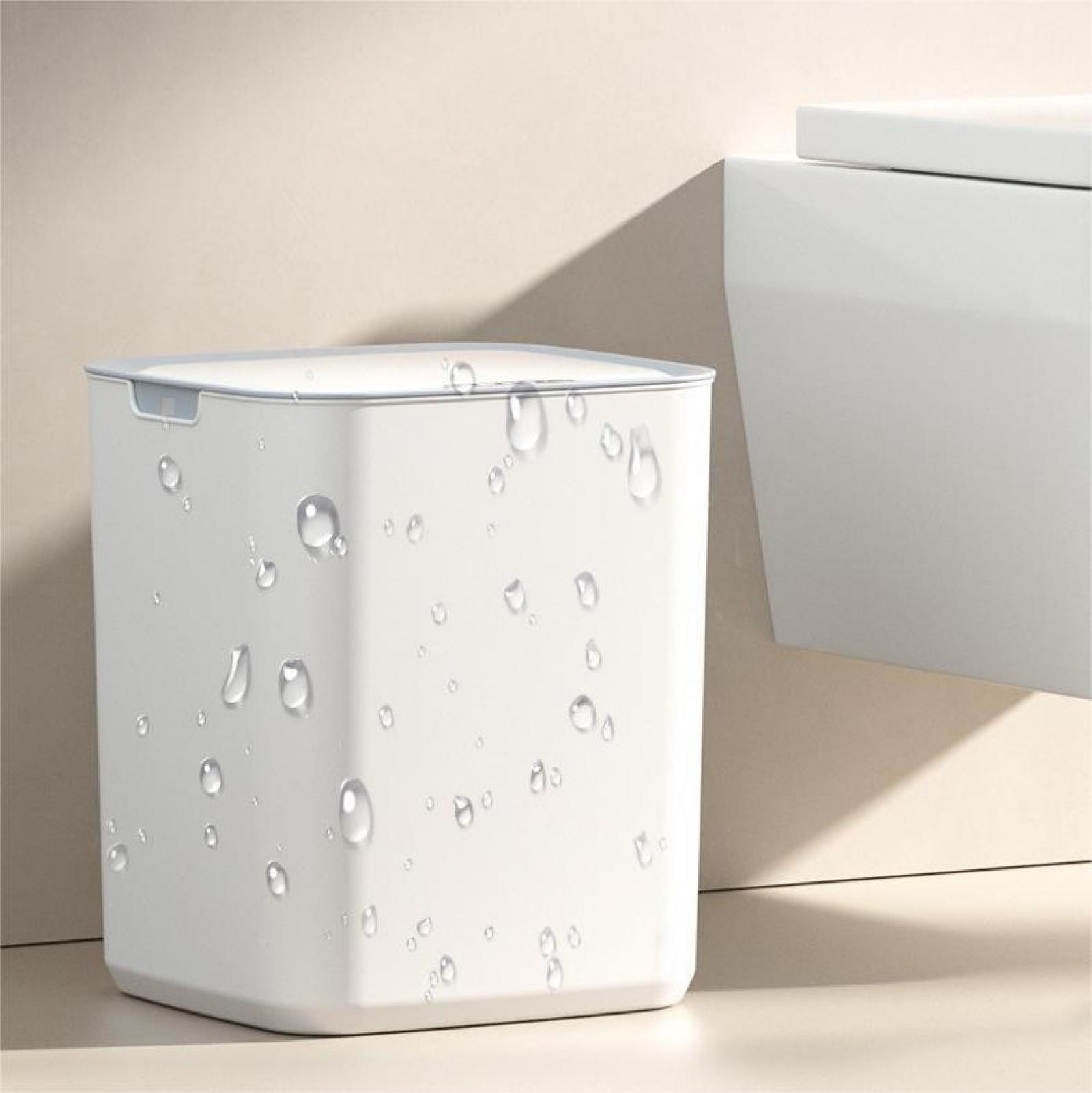 Ein weißer quadratischer Mülleimer mit Wassertropfen darauf, neben einem weißen Objekt und einer beigen Wand.