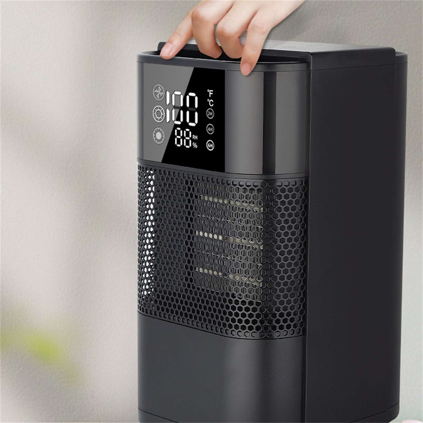 Ein schwarzer Elektroheizer mit digitaler Anzeige, eine Hand berührt die Oberseite. Anzeige zeigt Temperatur und Luftfeuchtigkeit.