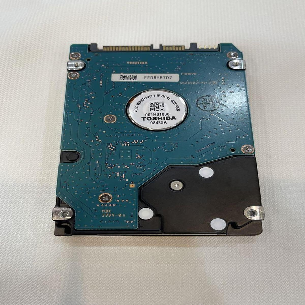 Un circuito stampato di un disco rigido Toshiba. Ha un circuito blu, un componente nero e un'etichetta bianca. Lo sfondo è bianco.