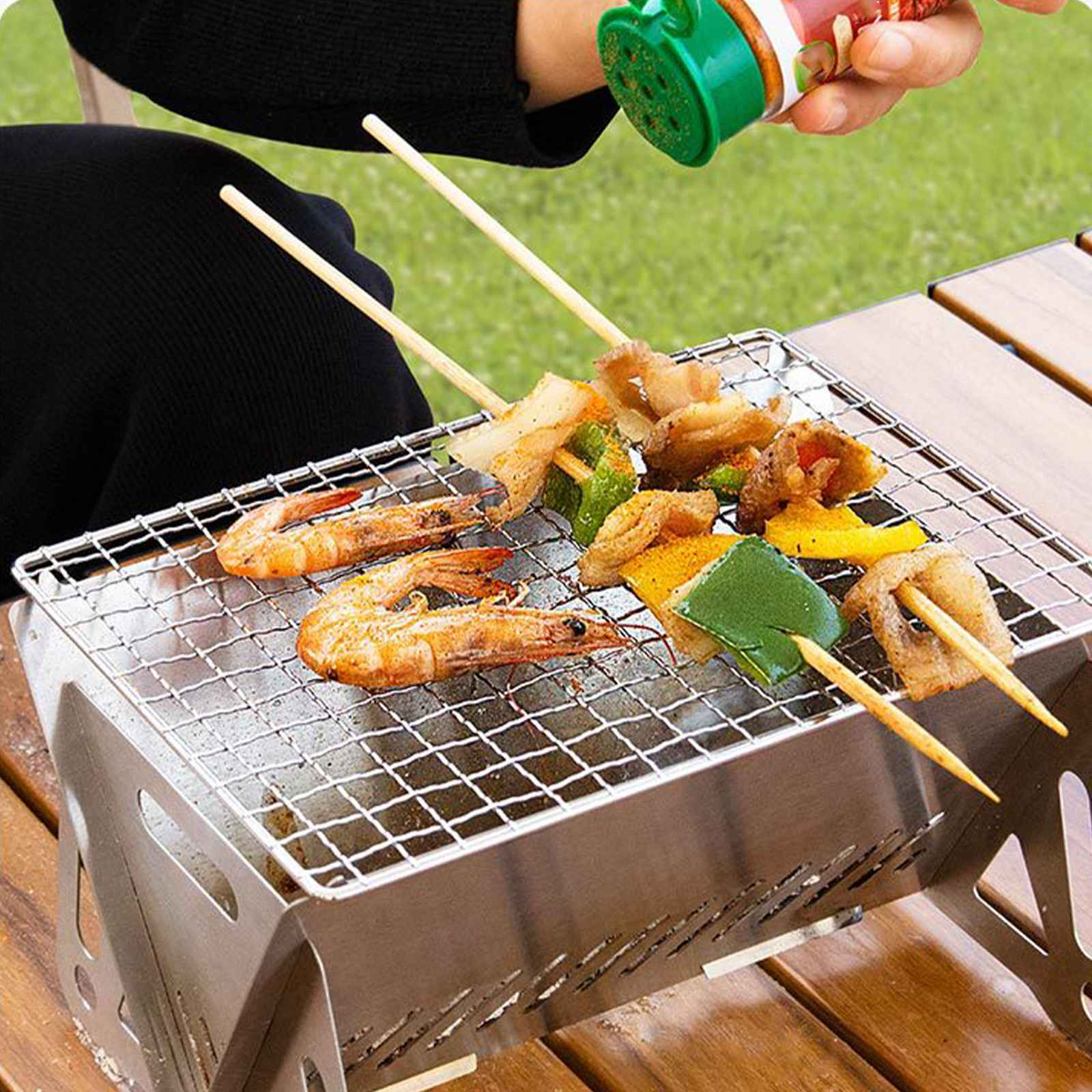 Ein Grill mit Spießen, Garnelen und Gemüse wird gewürzt. Eine Person hält einen Gewürzbehälter.