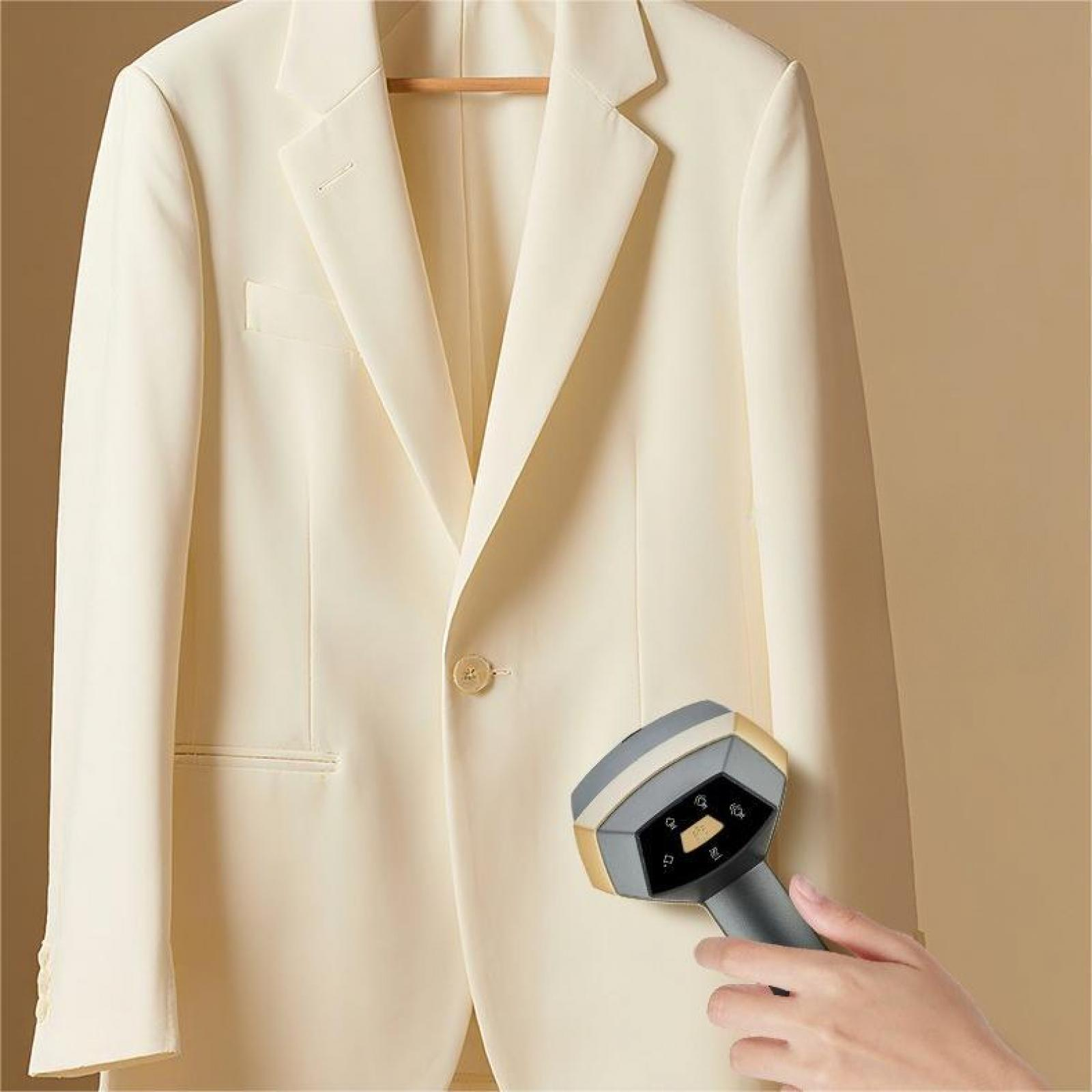 Ein cremefarbener Blazer hängt an einem Holzbügel. Eine Hand hält einen grau-goldenen Steamer, bereit, den Stoff zu glätten.