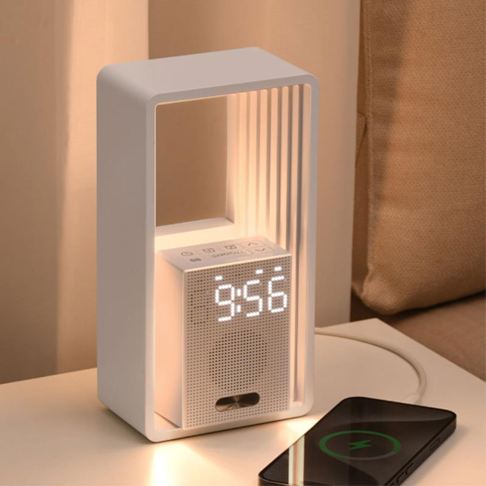 Eine weiße Nachttischlampe mit einer Uhr, die 9:56 anzeigt, und ein Telefon, das auf dem Tisch aufgeladen wird. Im Hintergrund ist ein beiges Sofa zu sehen.