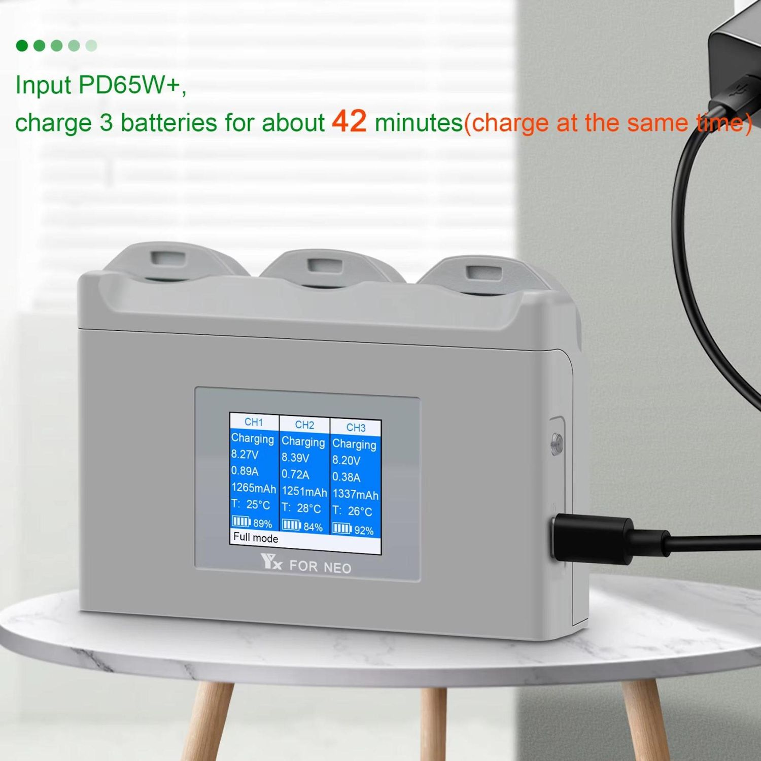 Un caricabatterie grigio con schermo che mostra lo stato di carica. Collegato a una fonte di alimentazione. Il testo indica la ricarica simultanea di tre batterie.