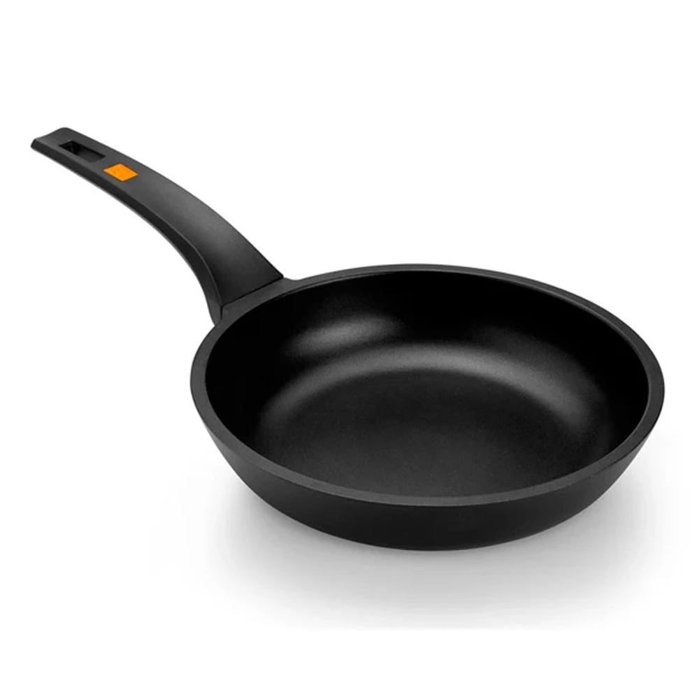 Una sartén negra con mango, detalle naranja, sobre un fondo blanco. La sartén está vacía.