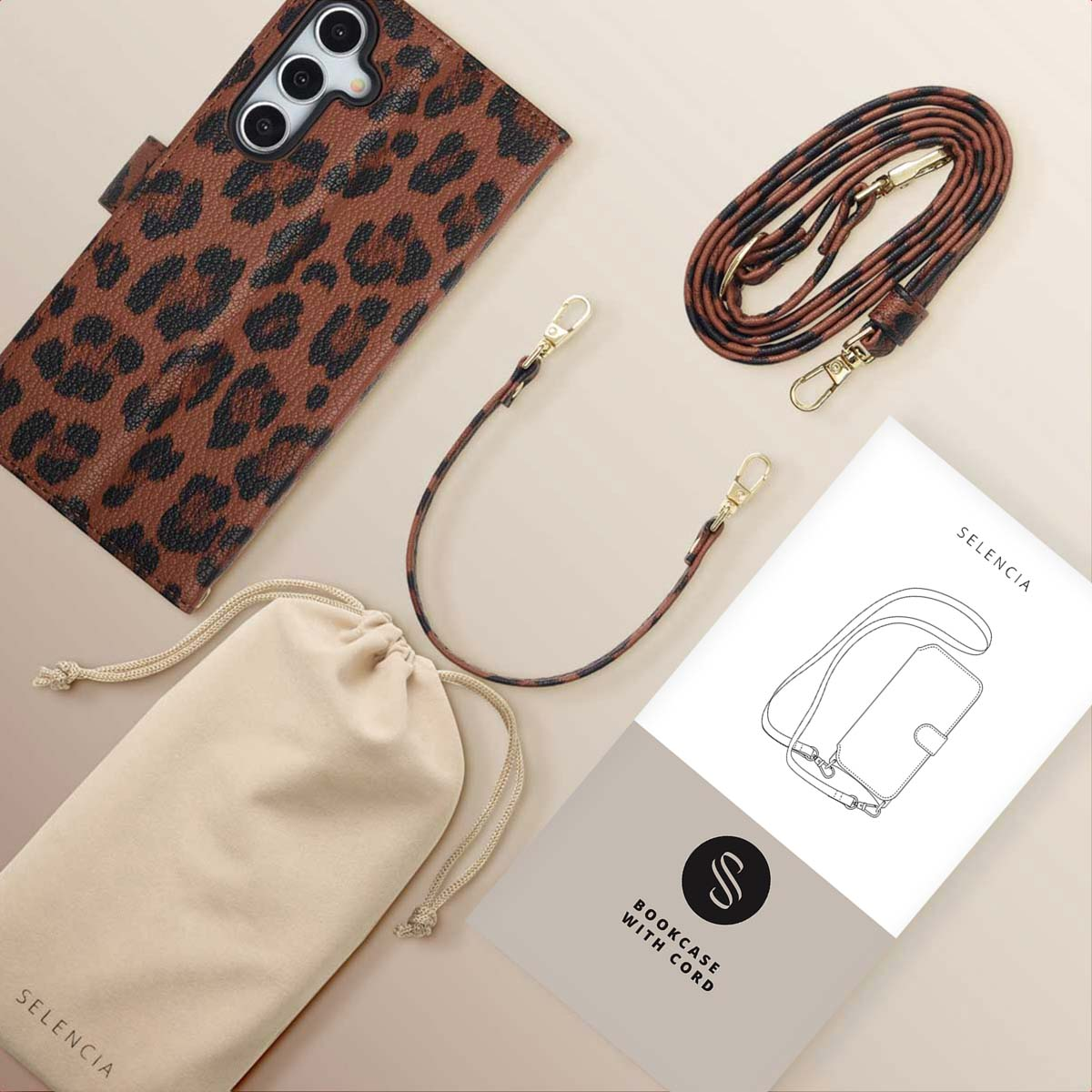 Een telefoonhoesje met luipaardprint, een schouderriem, een zakje en een handleiding liggen op een lichtbeige oppervlak.