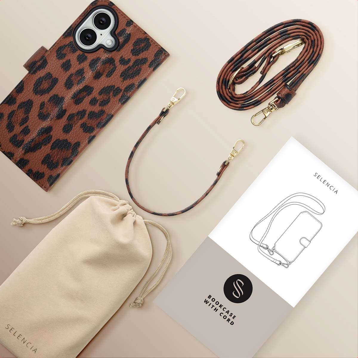 Custodia e cinturino per telefono con stampa leopardata, un astuccio beige e un libretto con un diagramma sono disposti su una superficie beige chiaro.