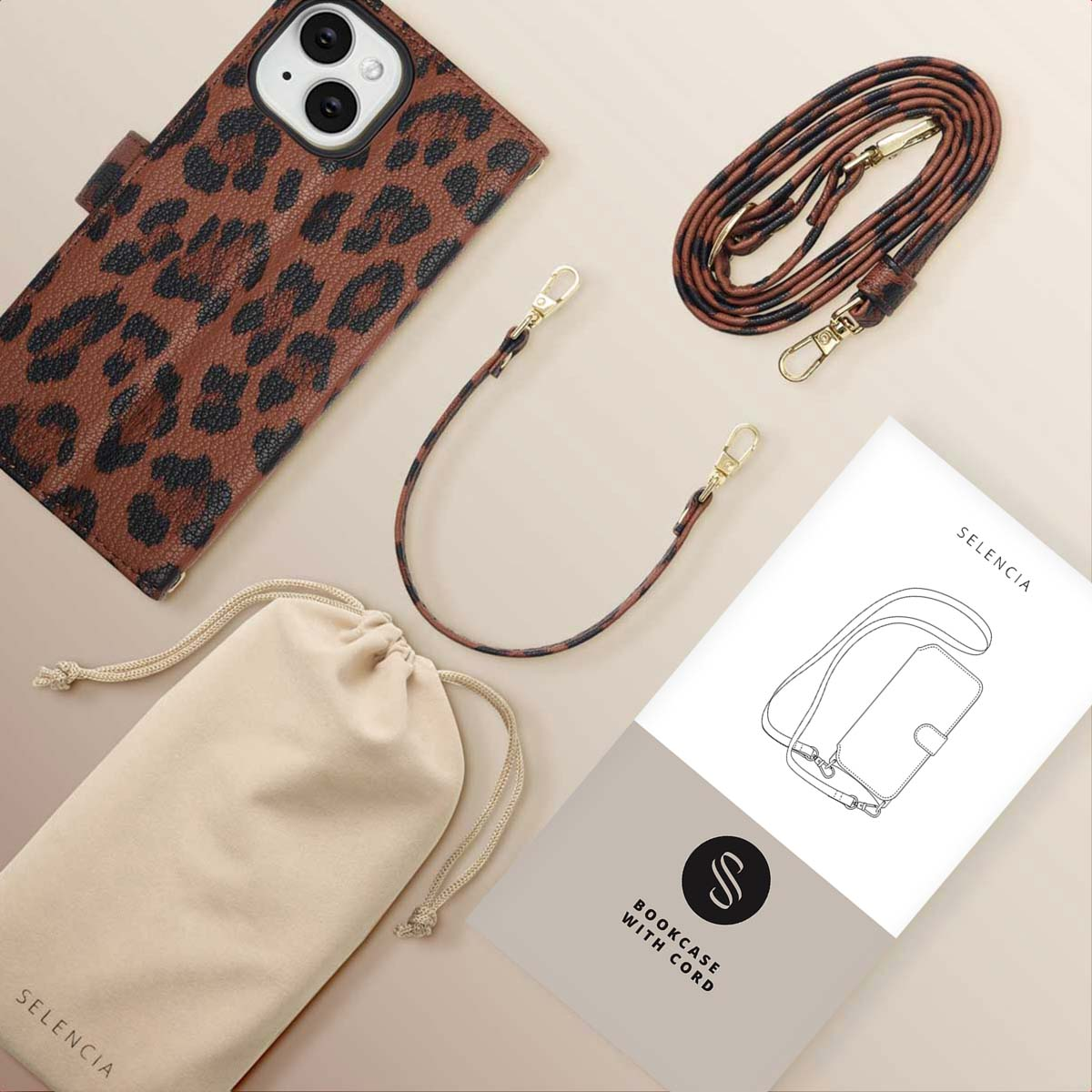 Een bruine telefoonhoes met luipaardprint, riem en etui met een boekje en koord. Items liggen op een lichtbruin oppervlak.
