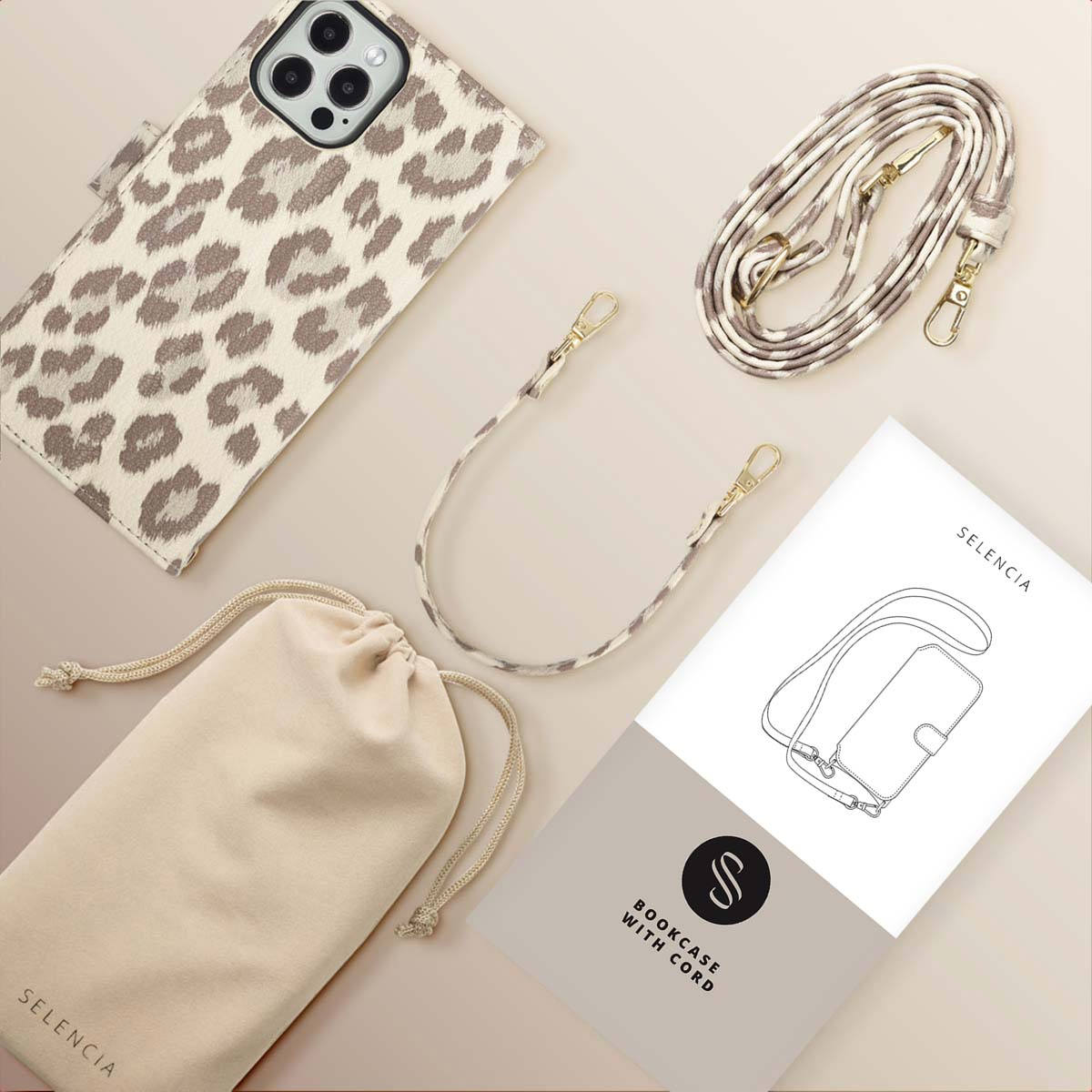 Une coque de téléphone à imprimé léopard, une sangle assortie, une pochette beige et un manuel sur une surface beige. La marque Selencia est visible.
